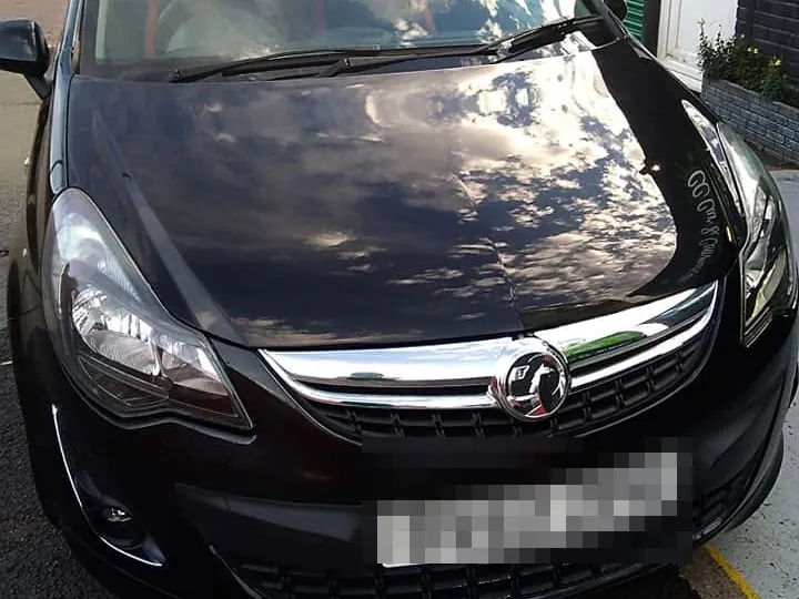 The same black Corsa outside the workshop, its bonnet and front end straight and gleaming