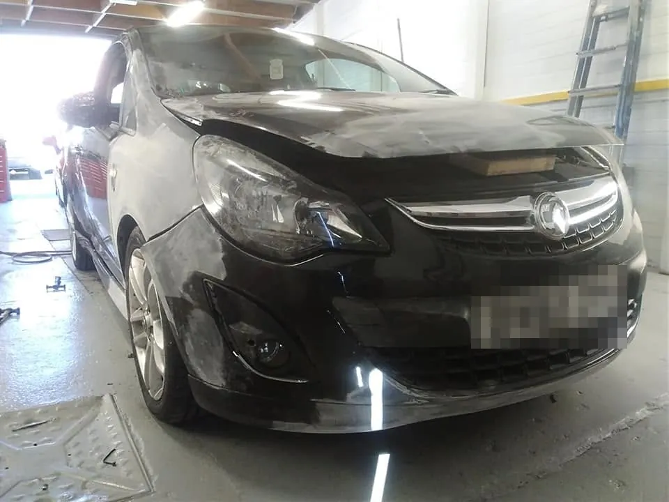 A black Vauxhall Corsa in the workshop with its bonnet buckled and its front wing crushed