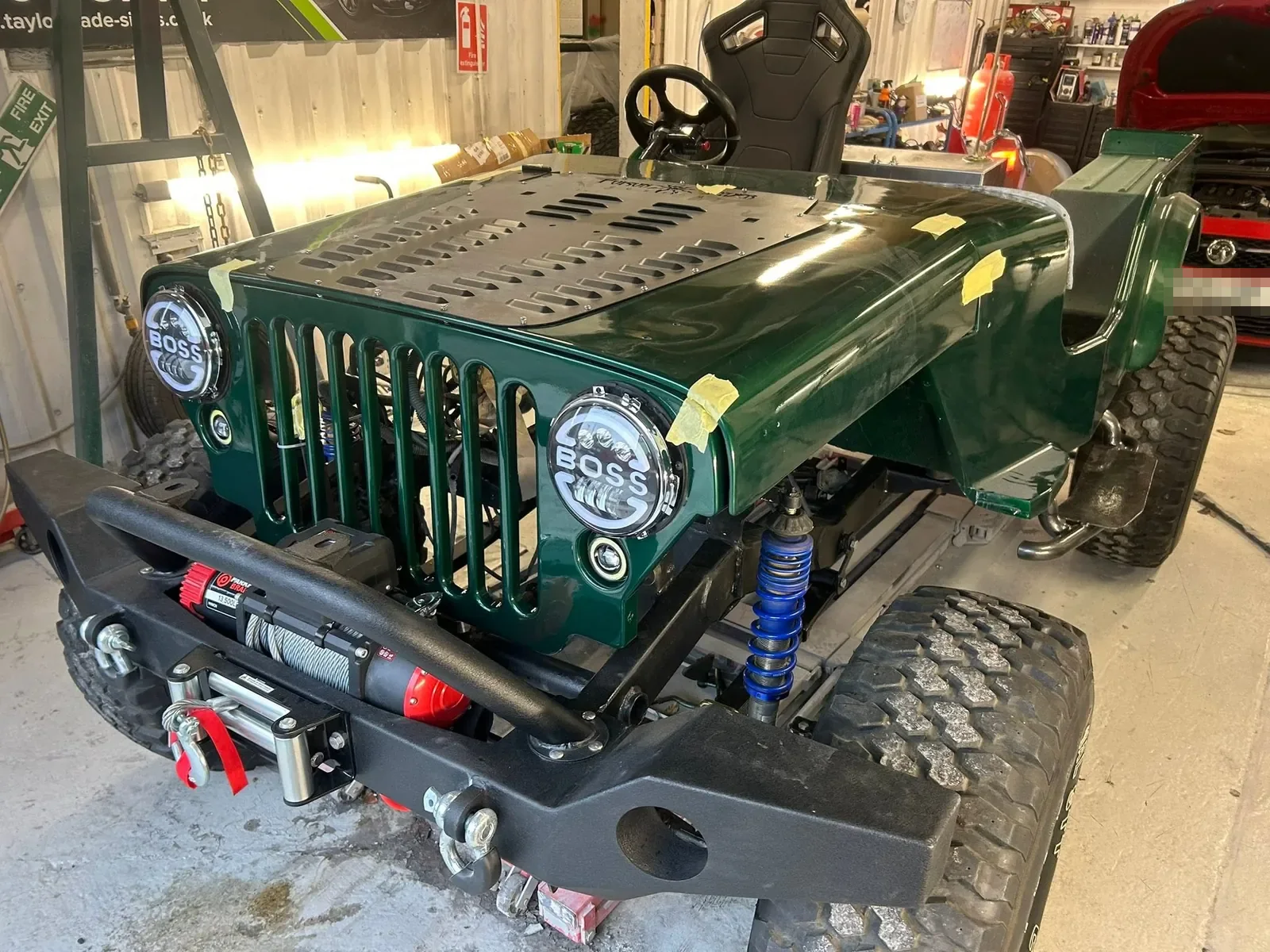 The same Jeep in the workshop, now dark green with a new black front bumper and winch, masking tape still on