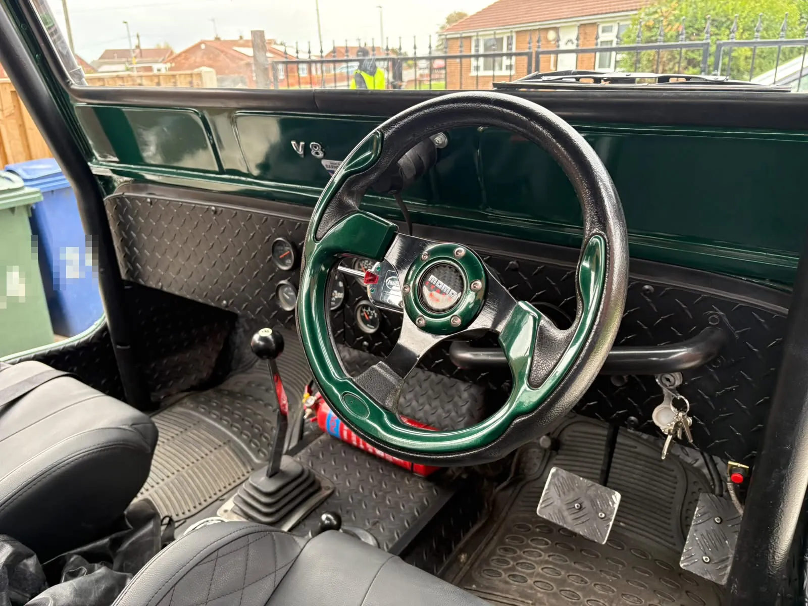 Inside the finished Jeep: a green and black steering wheel, a V8 badge on the green dash and chequer-plate panels