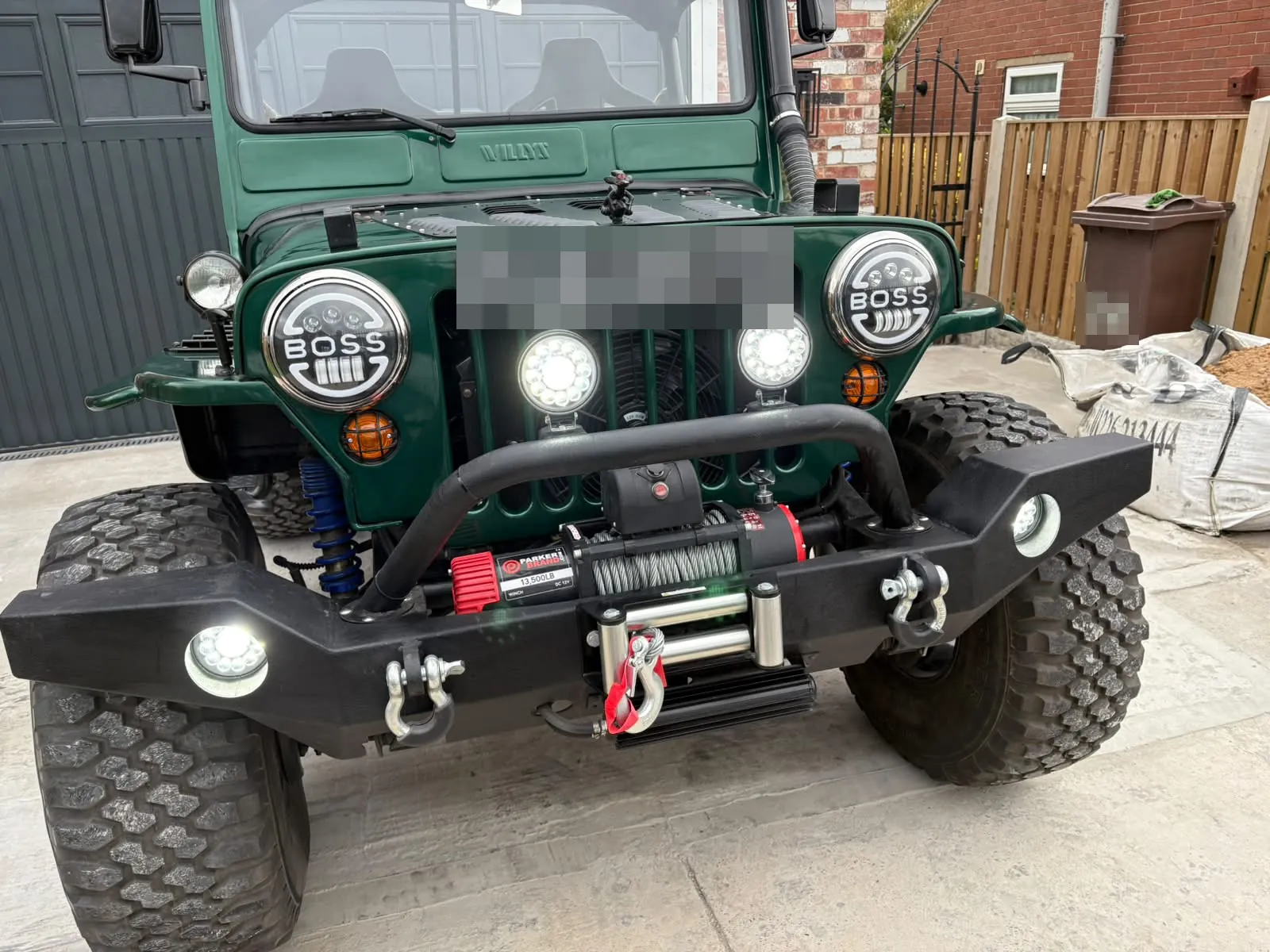The finished Jeep from the front, round headlights and spotlights lit, with a black bumper and winch