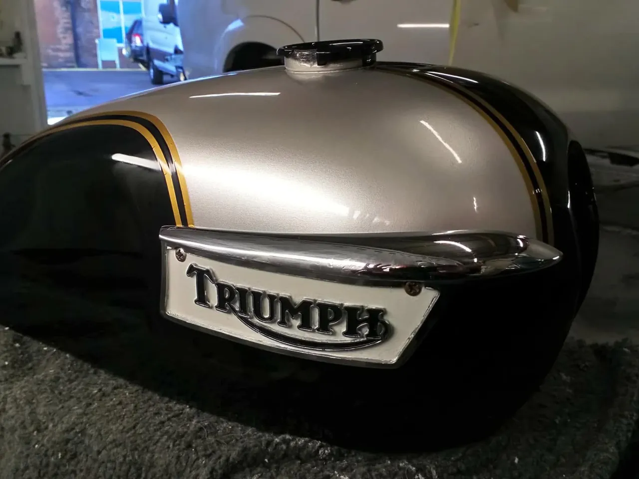 A Triumph motorbike fuel tank repainted in black and silver with gold pinstripes